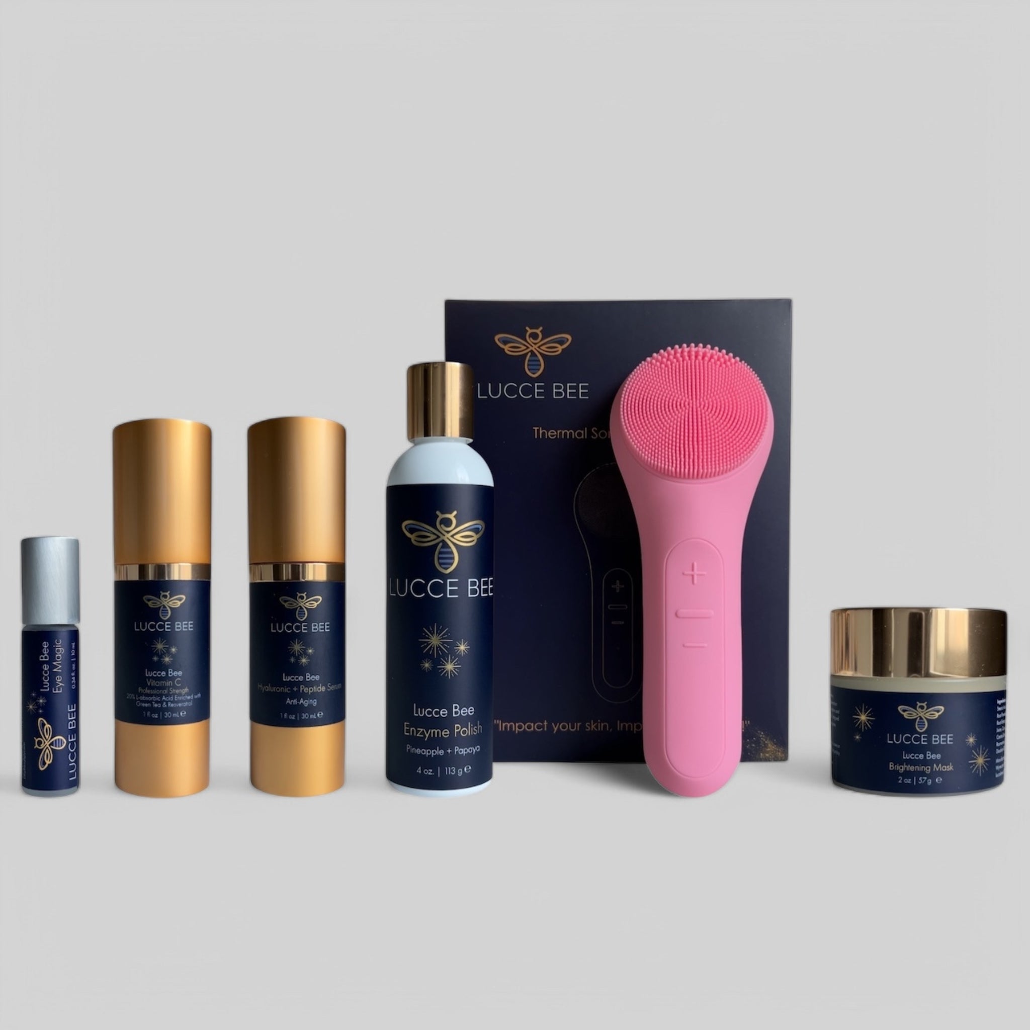 Lucce Bee skincare essentials bundle featuring Eye Magic, Vitamin C Serum, Hyaluronic + Peptide Serum, Enzyme Polish, Brightening Mask, and pink Thermal Sonic Facial Brush for glowing, healthy skin