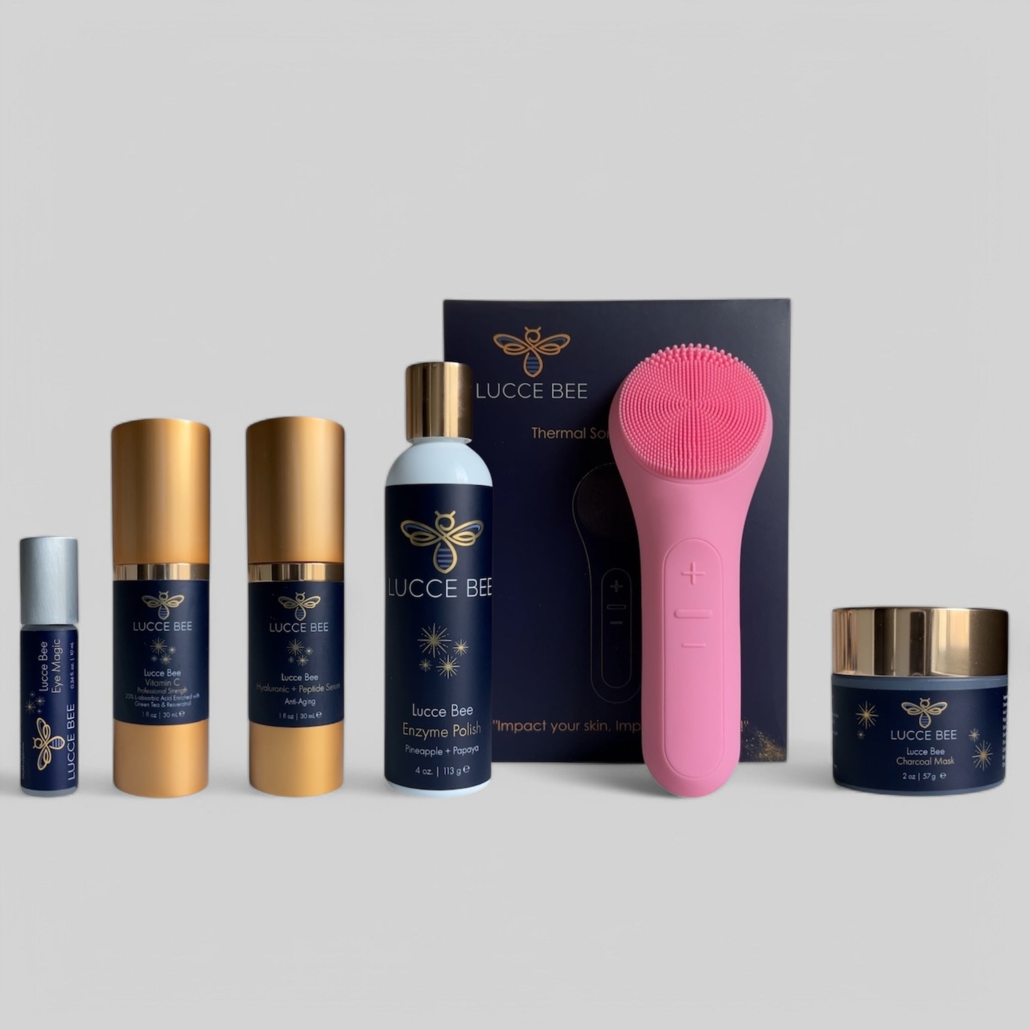 Lucce Bee skincare set featuring Eye Magic roller, Vitamin C serum, Hyaluronic + Peptide serum, Enzyme Polish, Charcoal Mask, and pink Thermal Sonic Facial Brush for deep cleansing and rejuvenated skin