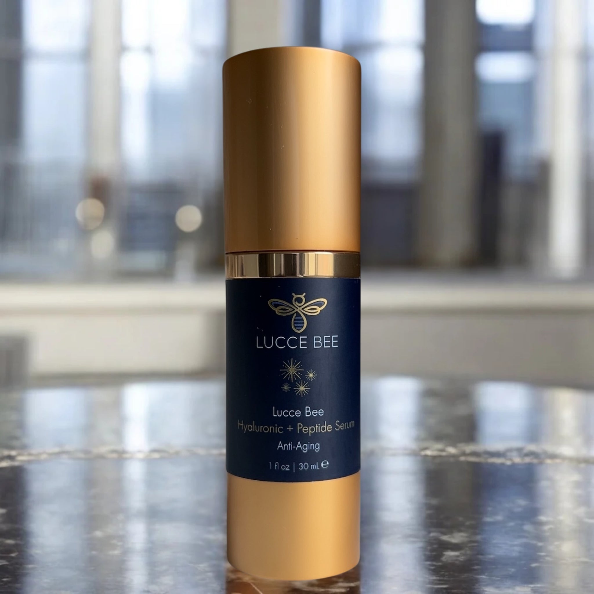 Lucce Bee Hyaluronic + Peptide Serum – Anti-Aging Hydration Treatment in Gold Bottle Displayed on Marble Countertop for Radiant, Plump Skin (1 fl oz / 30 mL)