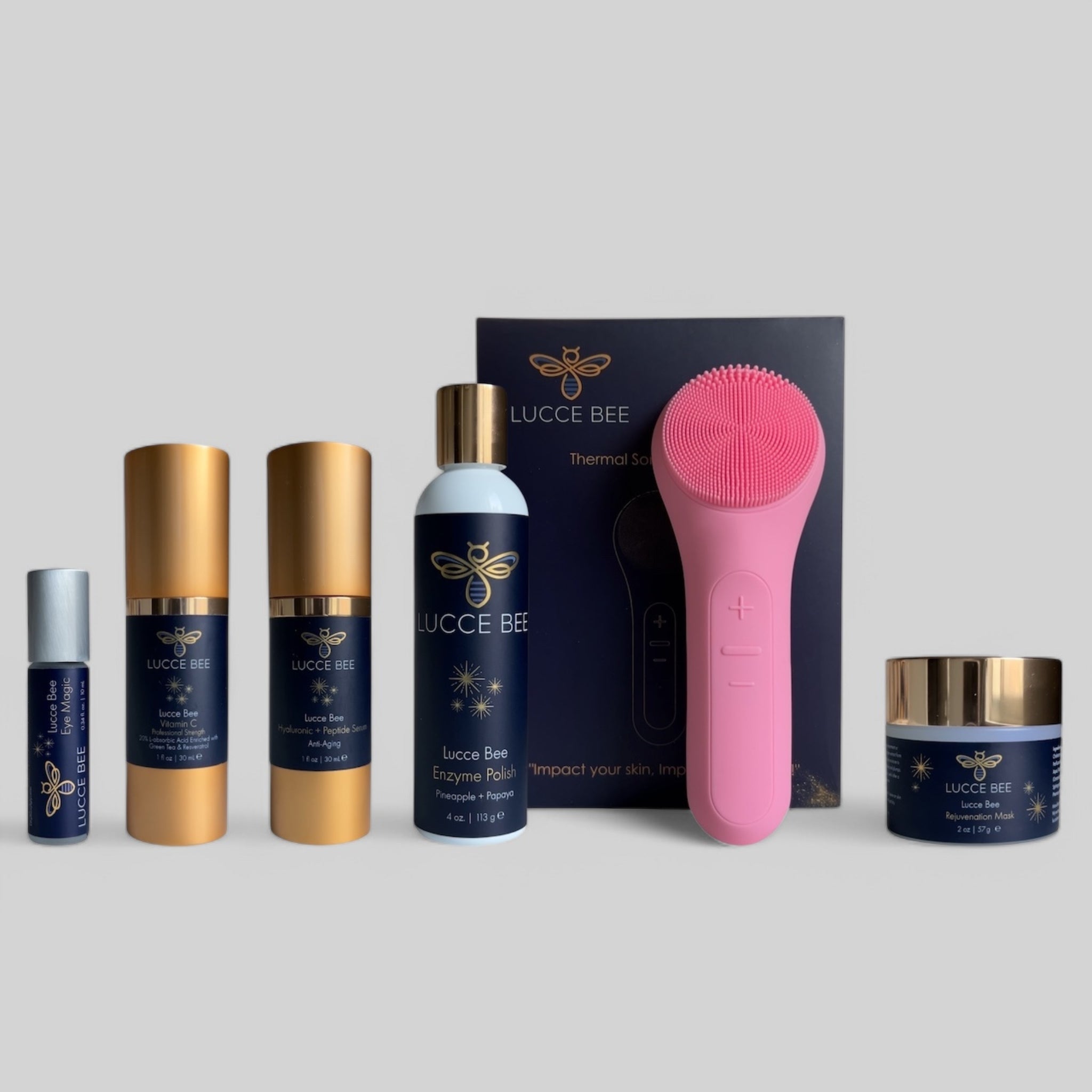 Lucce Bee skincare essentials set featuring Eye Magic, Vitamin C serum, Hyaluronic + Peptide serum, Enzyme Polish, Rejuvenation Mask, and pink Thermal Sonic Facial Brush — luxury skincare set for glowing, healthy skin